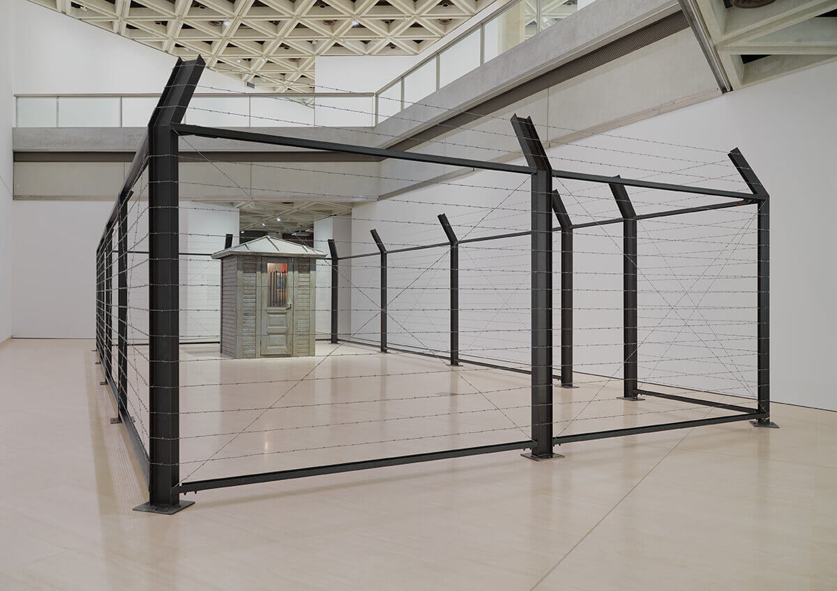 “Dışarı çıkmadık, çünkü hep dışardaydık / İçeri girmedik, çünkü hep içerdeydik”, (1995/2015) Yerleştirme ve ses, demir, dikenli tel, ahşap bekçi kulübesi, farklı boyutta renkli baskılar, çeşitli eşyalar ve Mp3 çalar. Arter Koleksiyonu. Hale Tenger, Arter ve AGWA izniyle.
